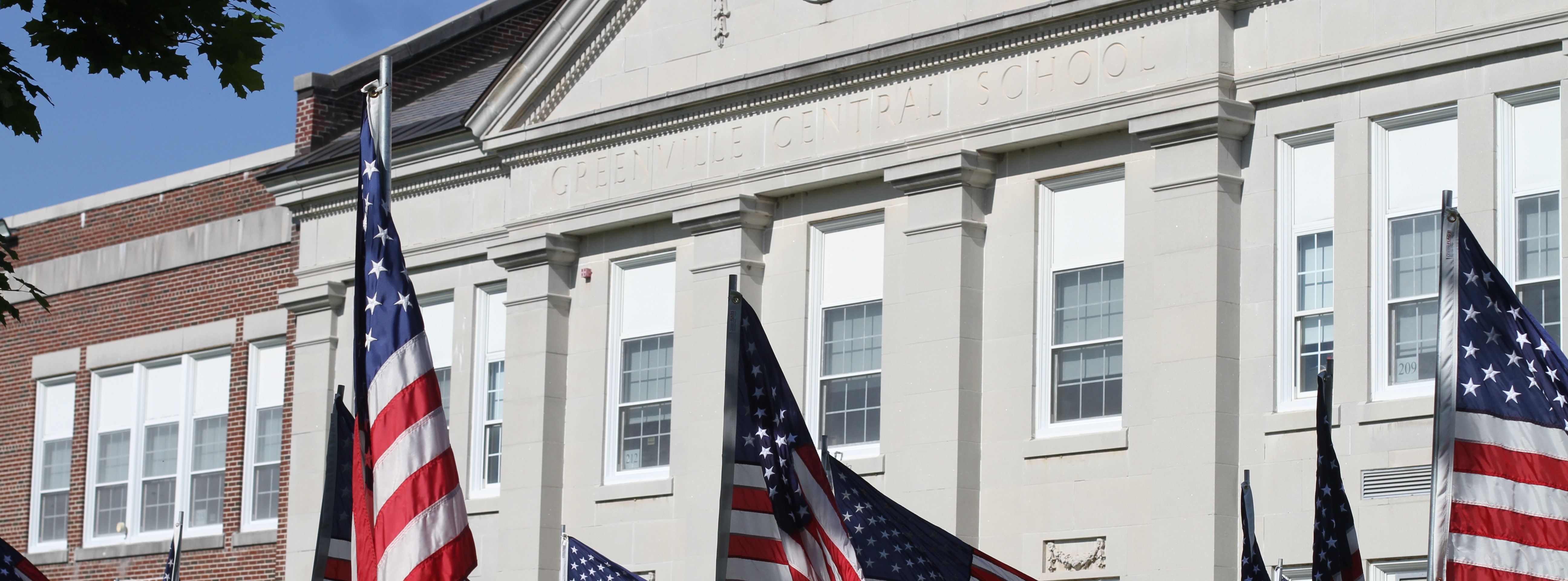 A line of American flags in front of a white building with multiple windows and a clock.