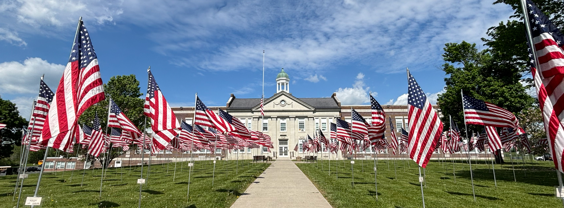 A pathway lined with American flags leads to a large white building. The flags are displayed on a grassy area.
