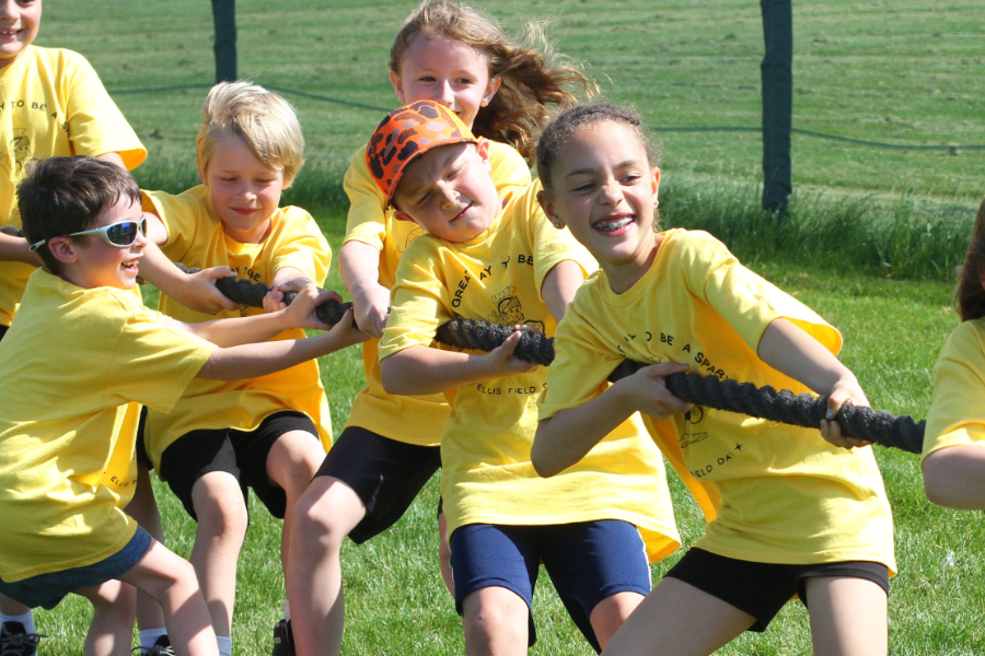 A group of children wearing yellow shirts participate in a tug-of-war in a grassy field.