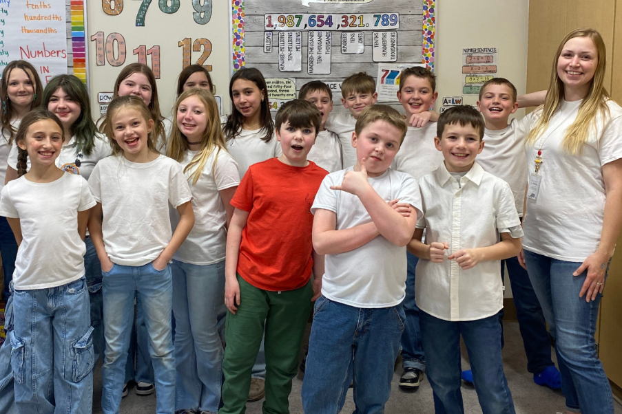 A classroom group of children and adults in white shirts and jeans posing for a photo.