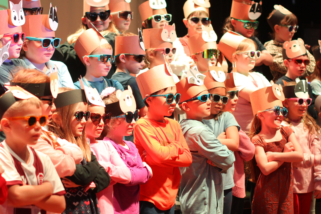 A large group of children wearing cone hats and sunglasses are standing in rows.