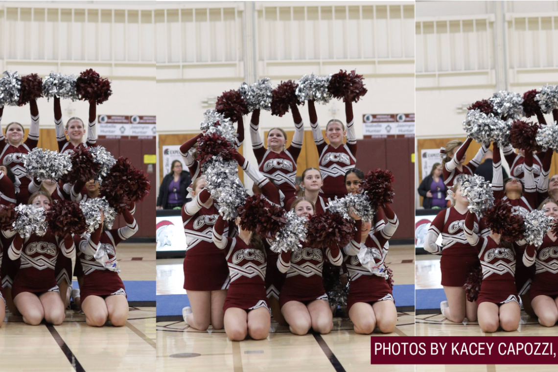 A group of cheerleaders in maroon uniforms with silver pom-poms posing in a gymnasium.