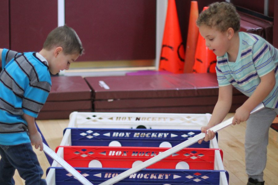 Two children playing with sticks and balls on a floor, one holding a stick, and the other with a basket.