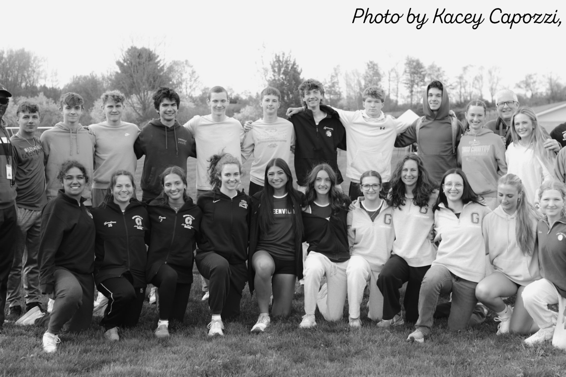 A group of individuals in athletic wear pose for a photo on a grassy field with trees in the background.