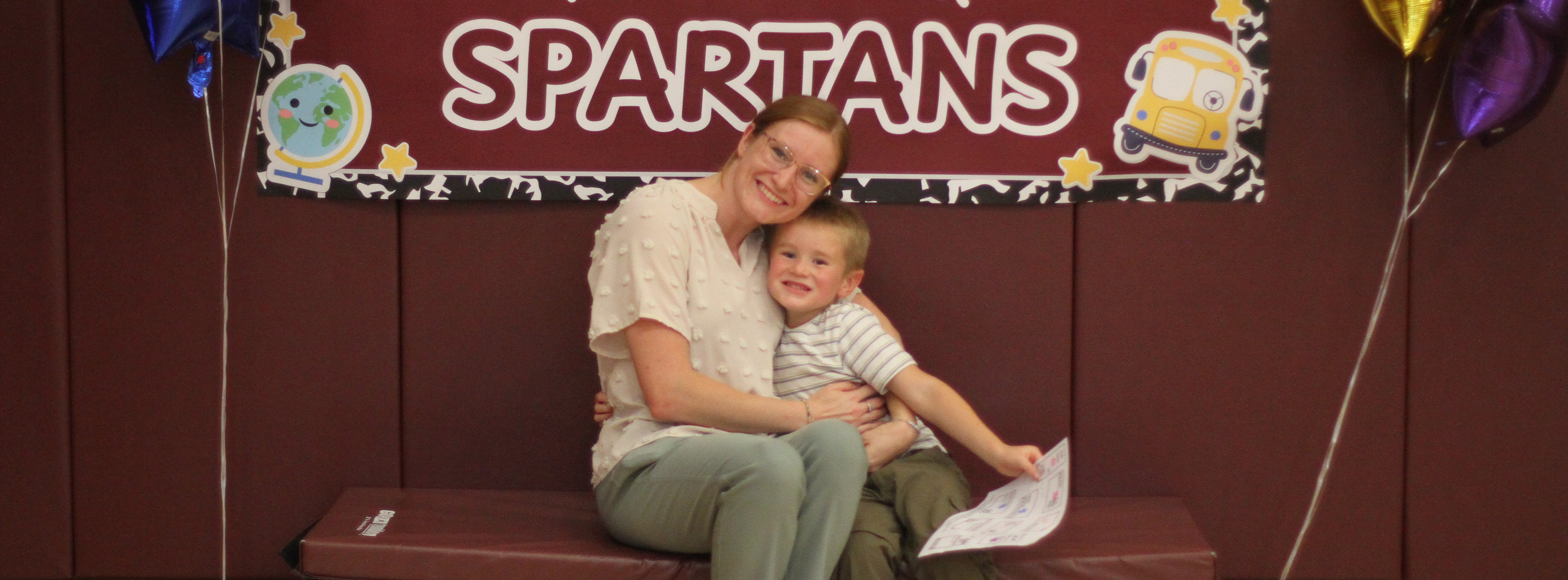 A woman and a young boy sit on a bench in front of a welcoming banner.