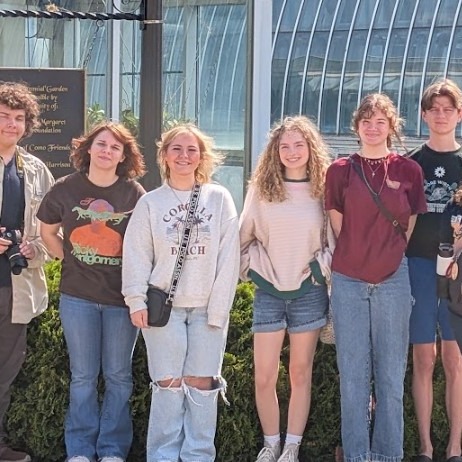 Student lined up smiling at camera in sunshine. They are standing in front of a domed conservatory/greenhouse structure
