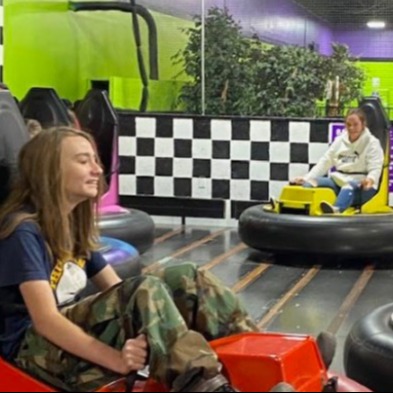 Student smiling in foreground in bumper car, staff also in background of picture in bumber car