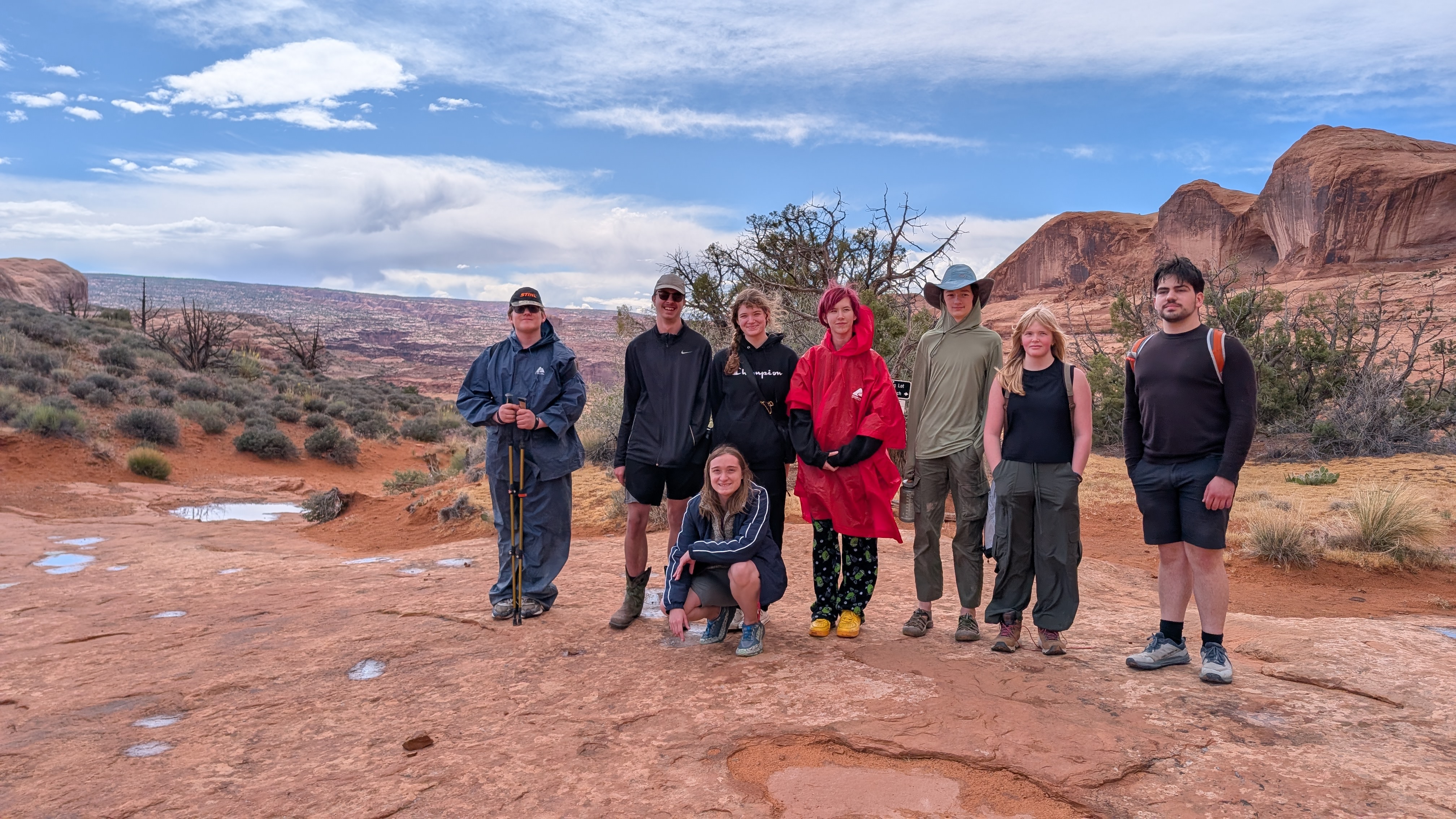 8 Students smiling at camera with background of arches national park in Utah
