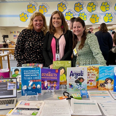 Three teachers presenting their research with a table filled with children's picture books