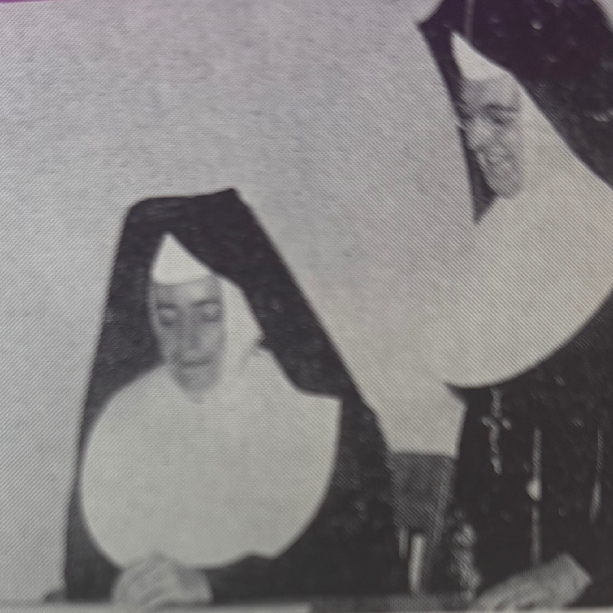 An open book displays a black and white photo of three nuns, with text below identifying them.