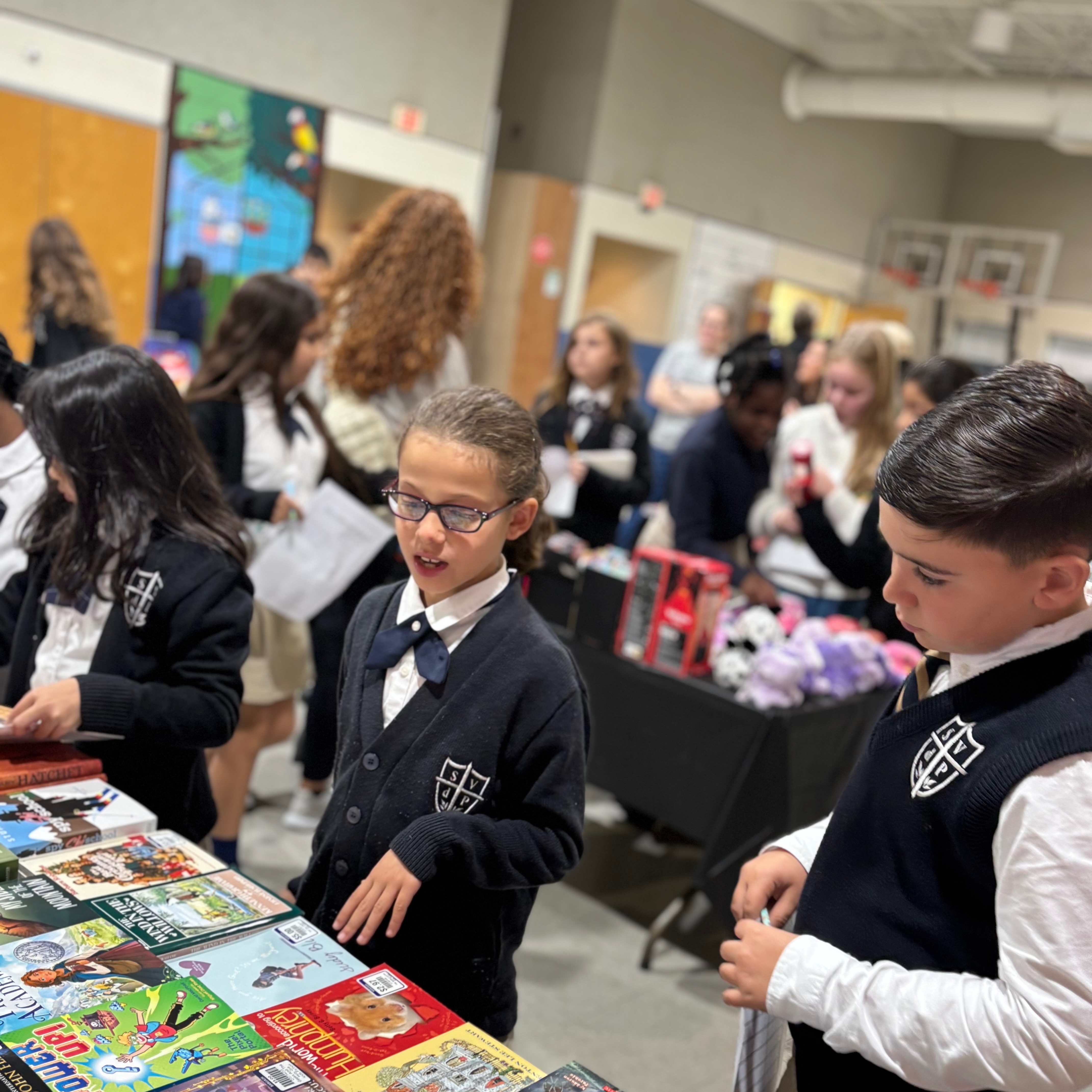 Children in school uniforms browse a table full of books, with others standing in the background.