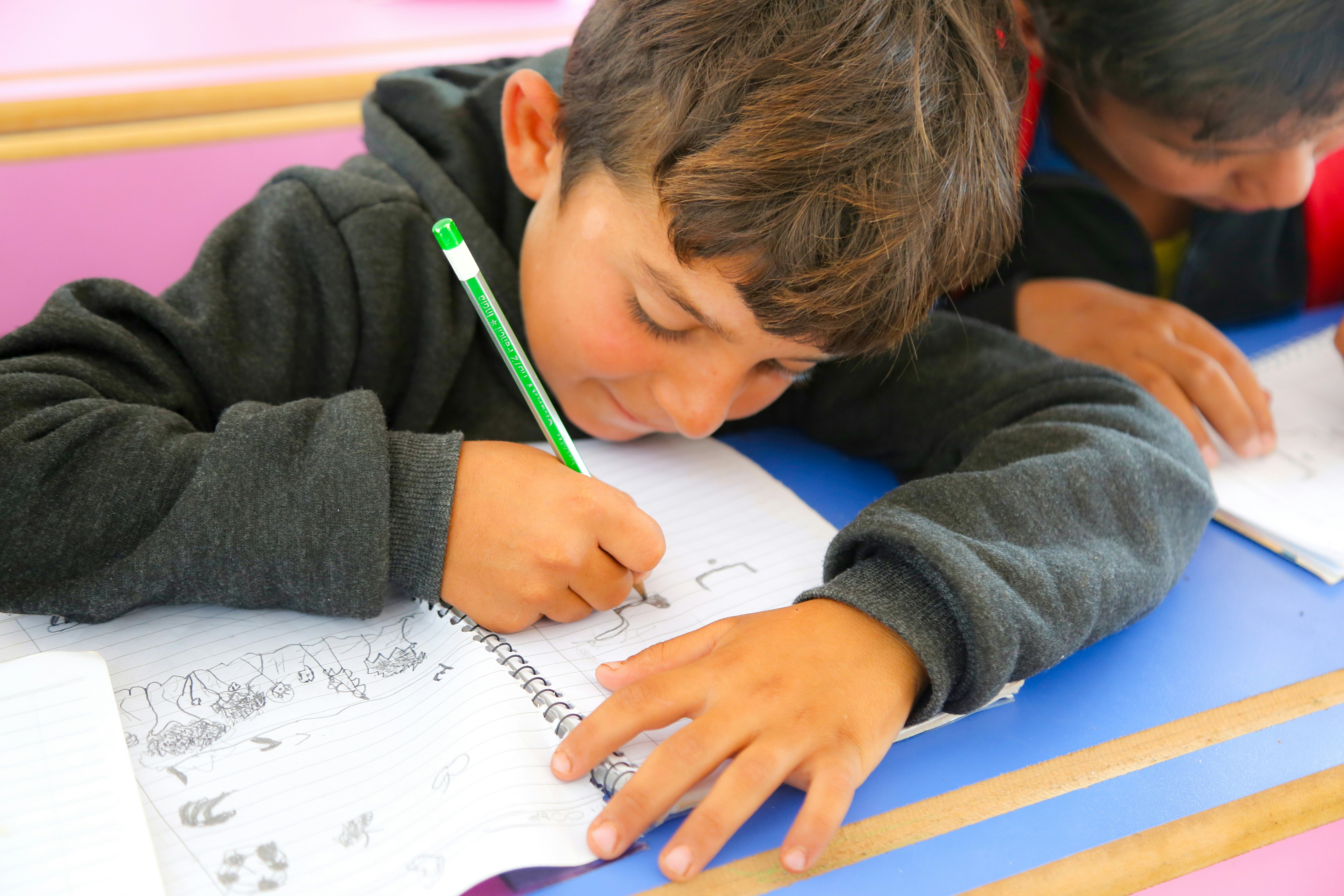 Image of young boy, drawing on a notebook with a friend next to him