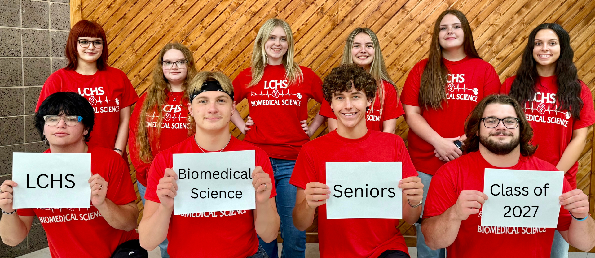 A group of students in red shirts pose for a photo, holding signs reading "Biomedical Science Seniors Class of 2027".