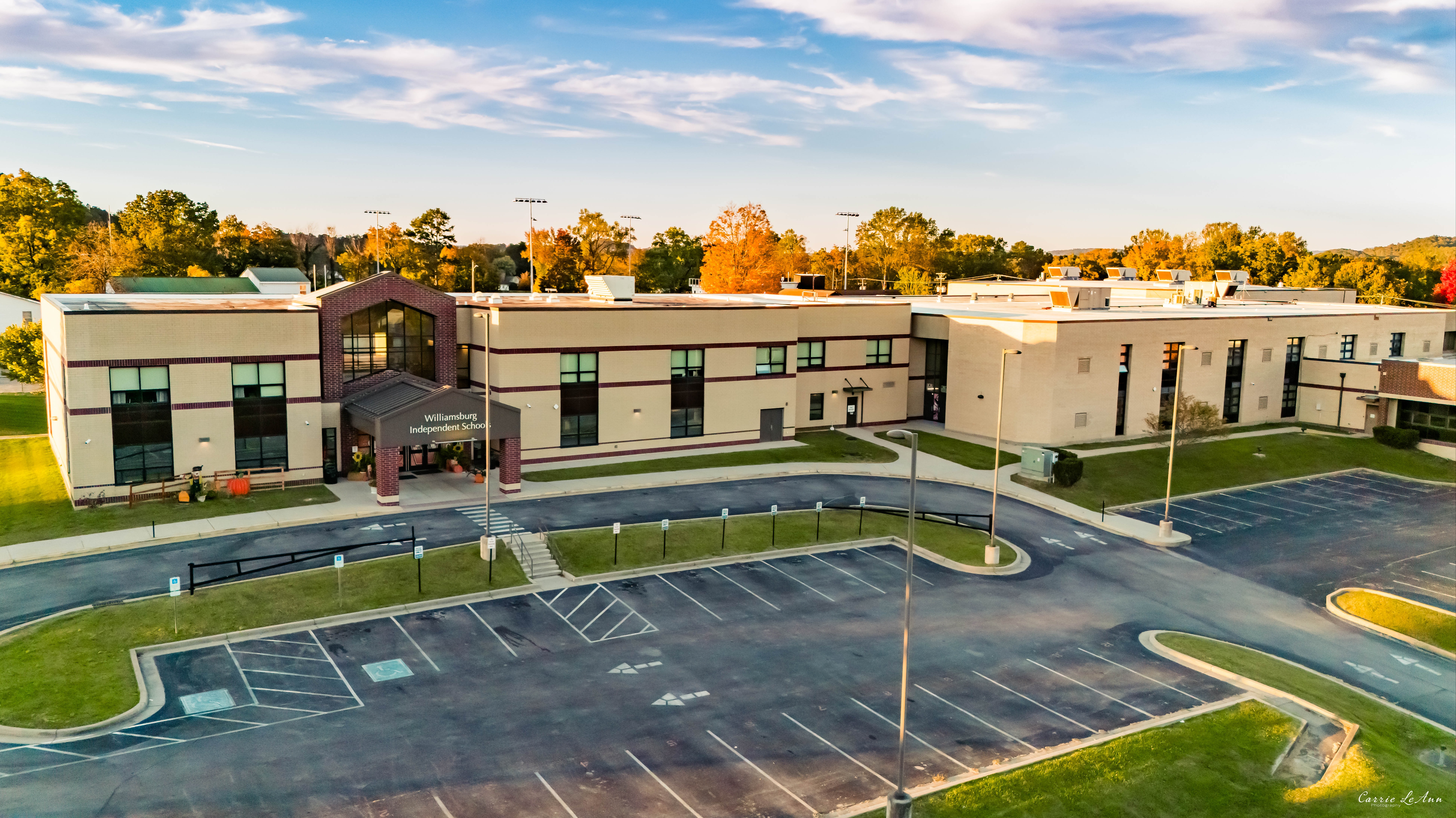 An aerial view of a large building with parking lot, green grass, and trees in the distance.
