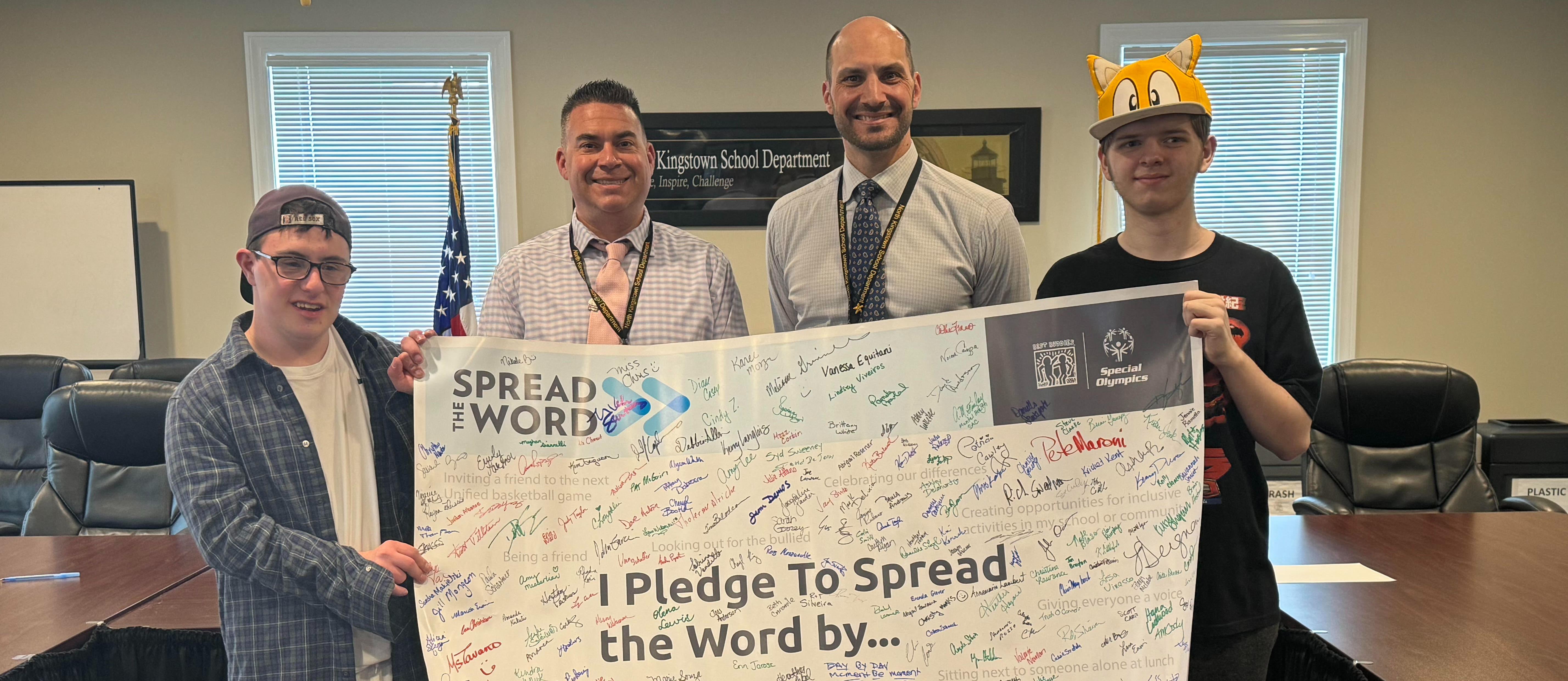Students and staff holding a signed banner that reads "I pledge to spread the word by..."