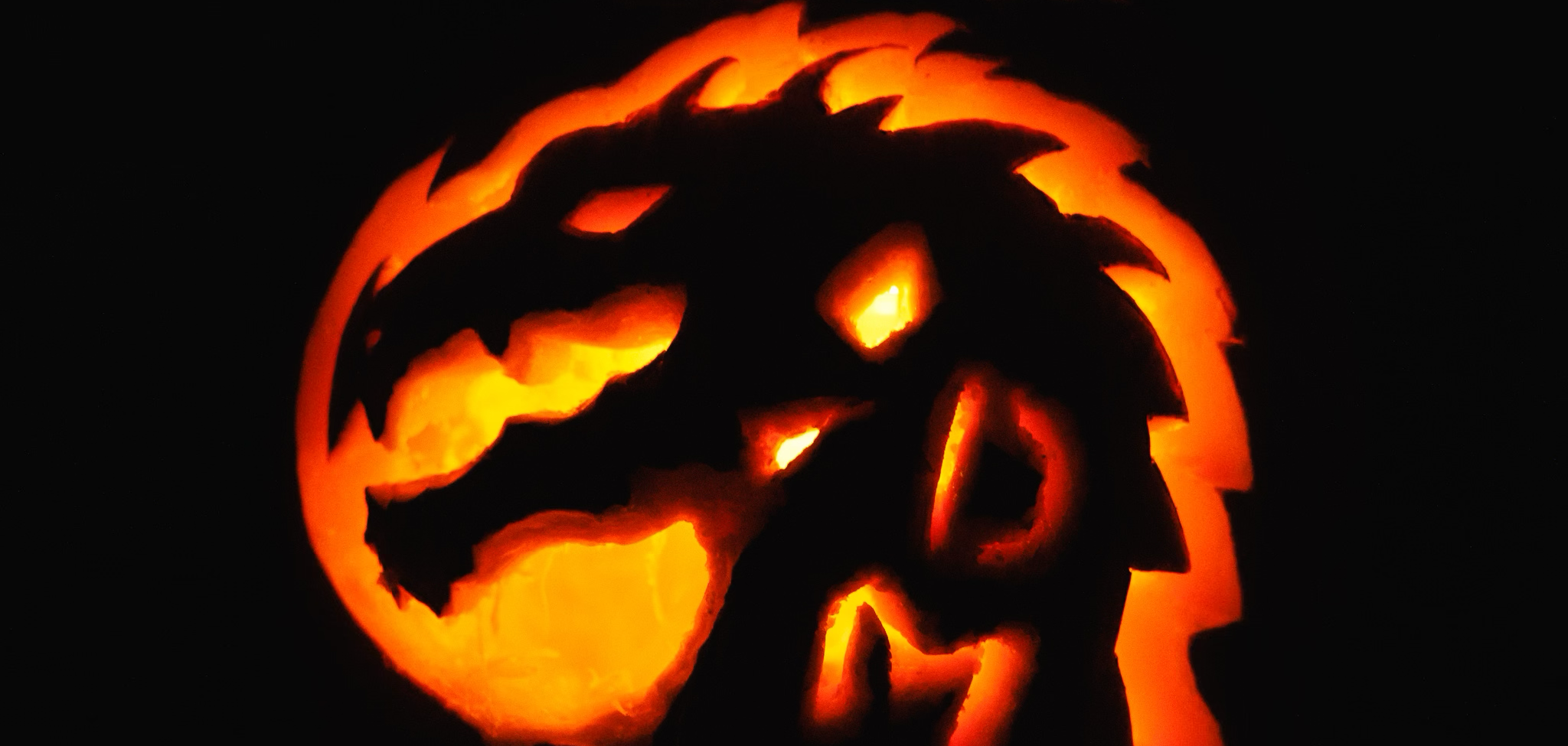 A carved pumpkin with a dragon design, illuminated from within, showcasing intricate details. The pumpkin is in a dark setting.