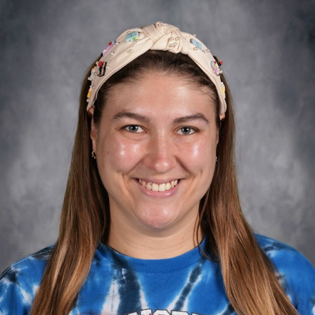 A woman with long dark hair wears a blue tie-dye shirt with "Johnsburg" in white letters.