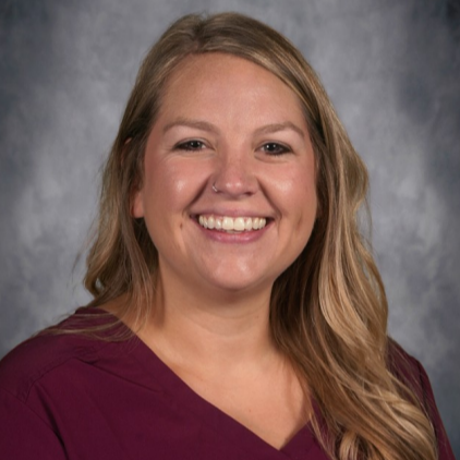 Woman with blonde hair, wearing a maroon shirt, smiling and facing the camera.