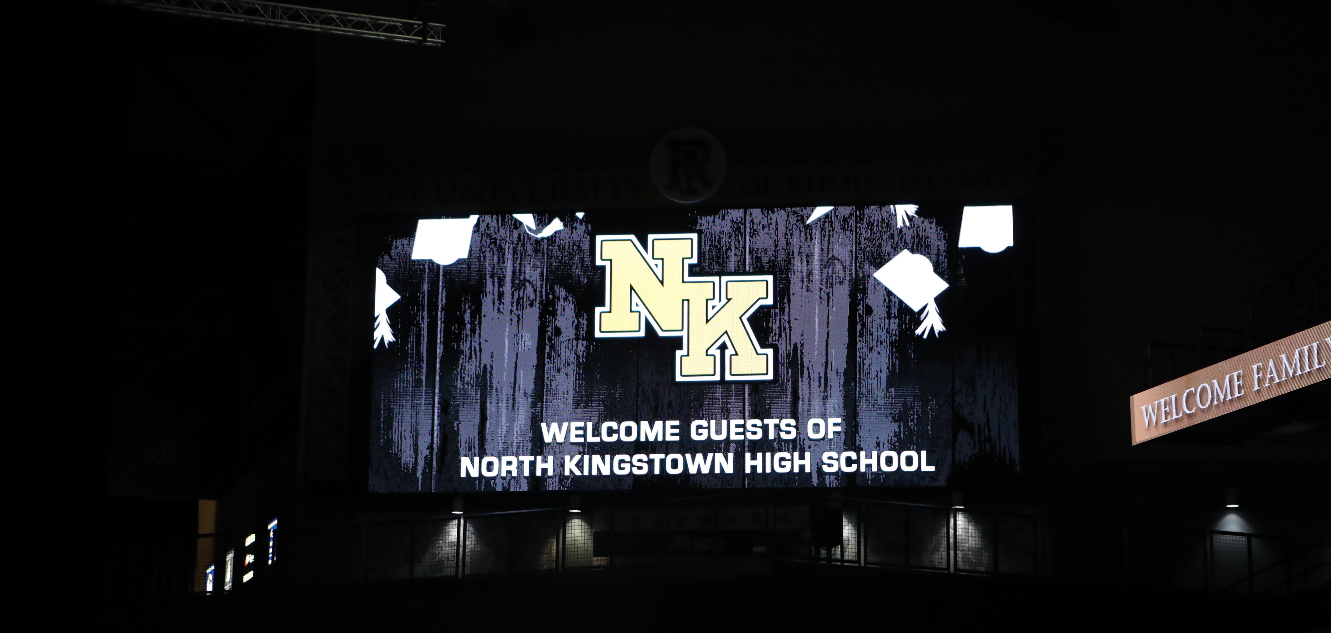 A large screen displays "NK" and "WELCOME GUESTS OF NORTH KINGSTOWN HIGH SCHOOL" against a dark background.