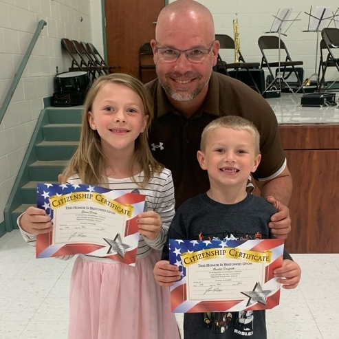 Principal poses with two smiling students receiving award