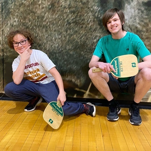 Two young men pose with ping-pong paddles in gym