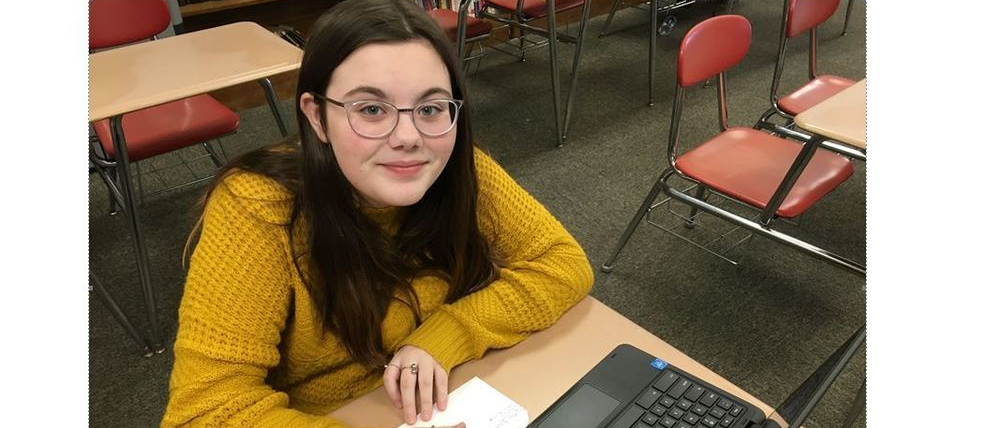Student in a yellow shirt and glasses works on a laptop