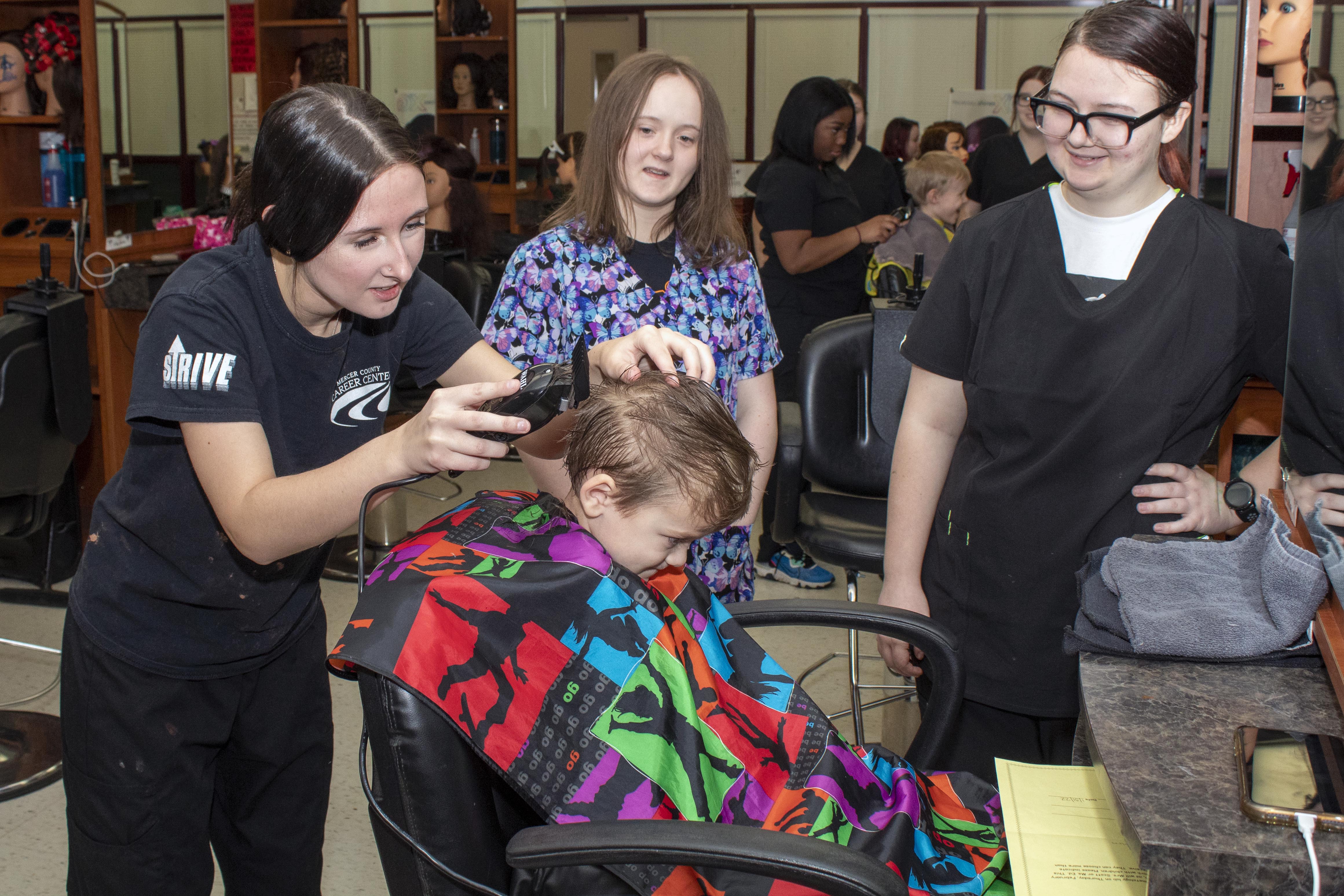 Cosmetology students style the hair of an MCCC Preschool toddler as a Early Childhood Student Teacher looks on.