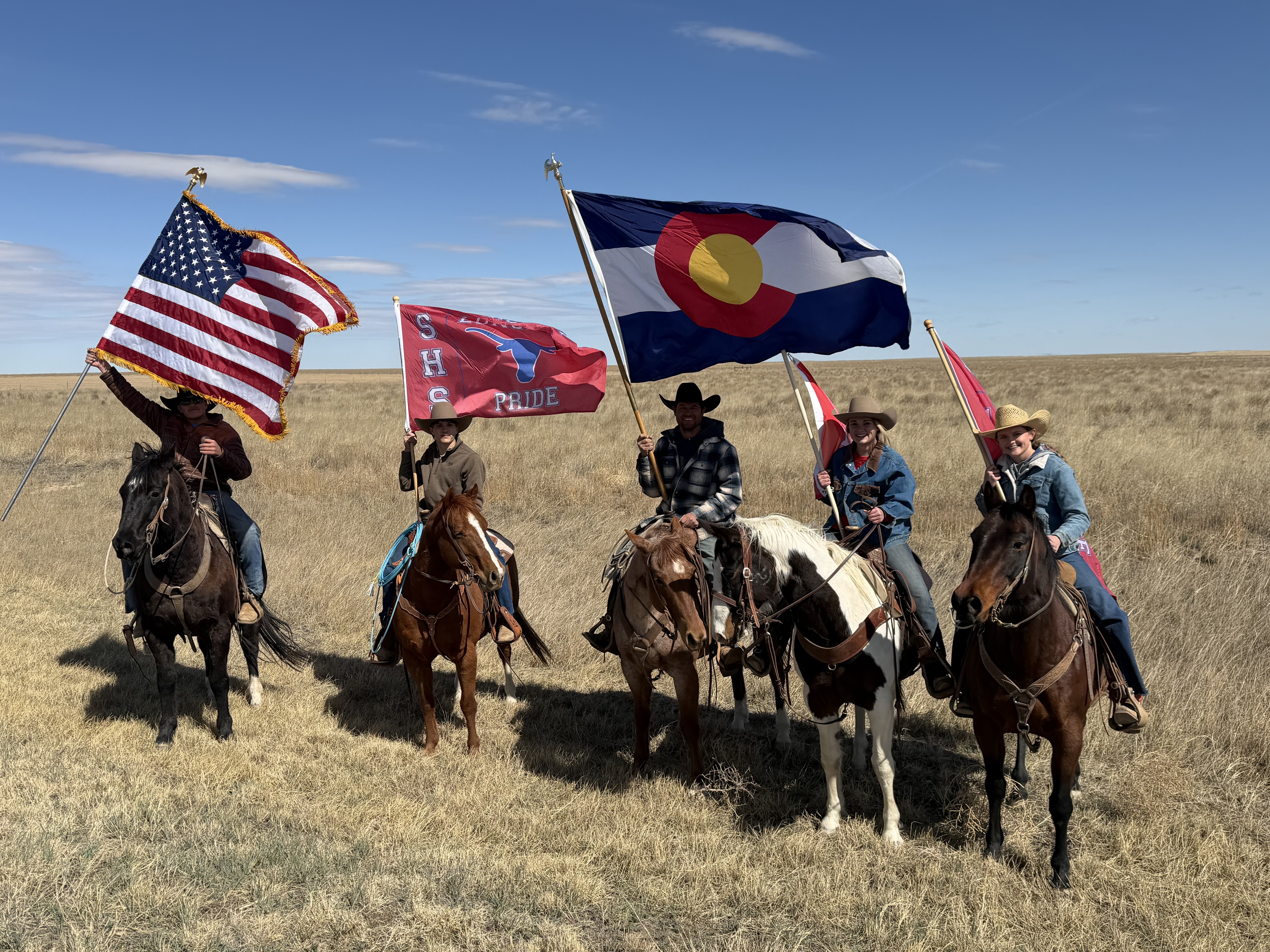 picture of 5 people riding horses and holding US, Colorado, and Springfield Longhorns flags