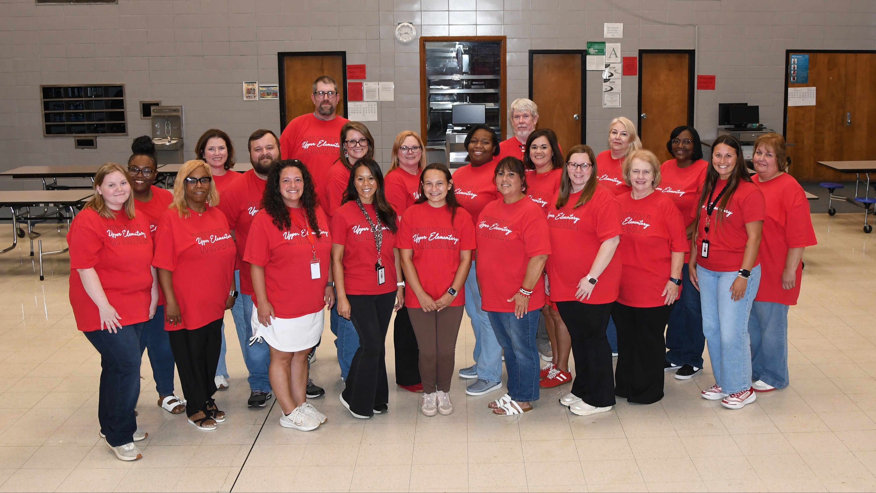 A group of people in red shirts and jeans pose for a picture in a room with white walls.