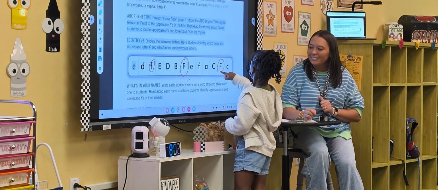 student working on letters with a teacher with a smart board