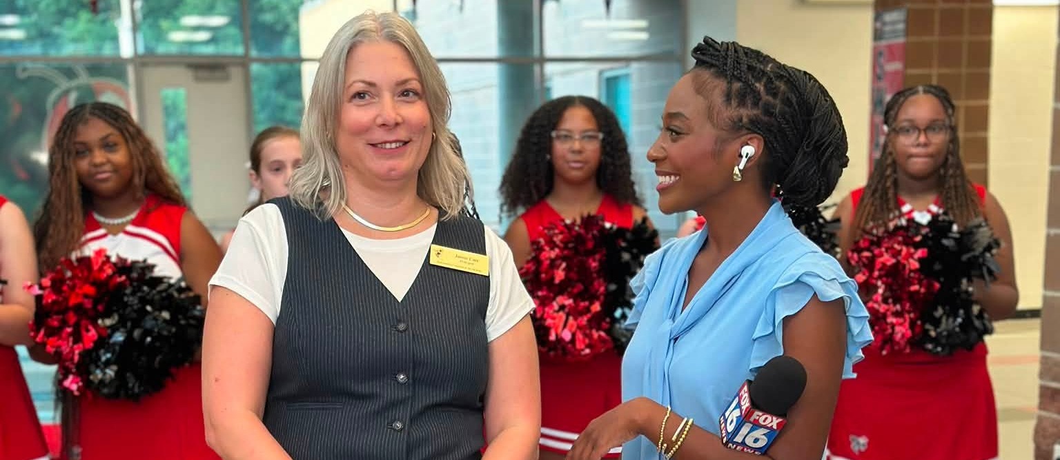 Principal Janna Carr with an interviewer and cheerleaders