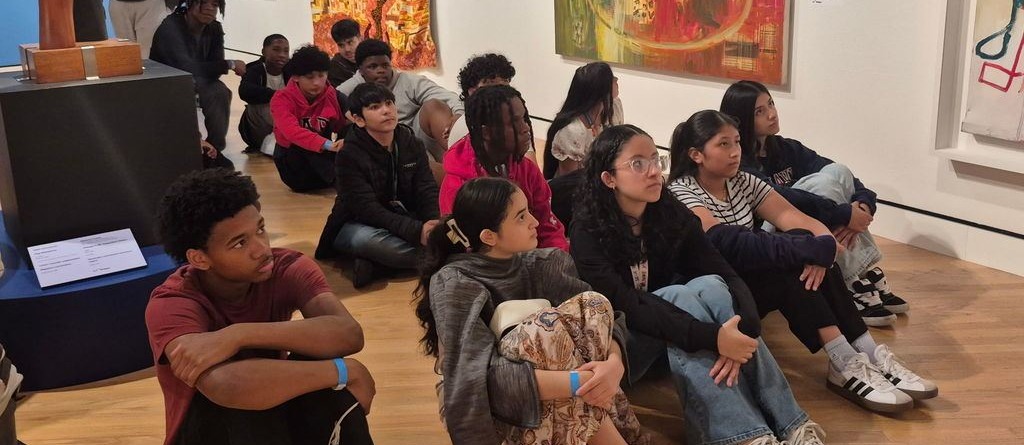 Students sitting on the floor listening intently.