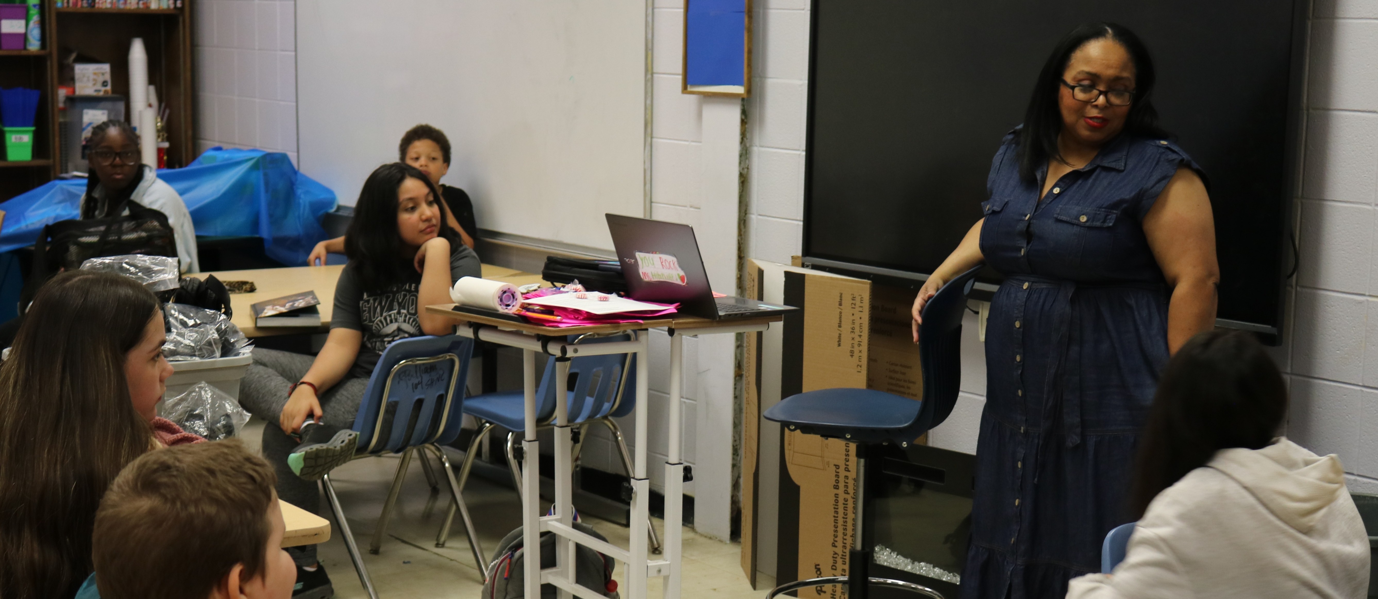 A classroom with students listening to a teacher.