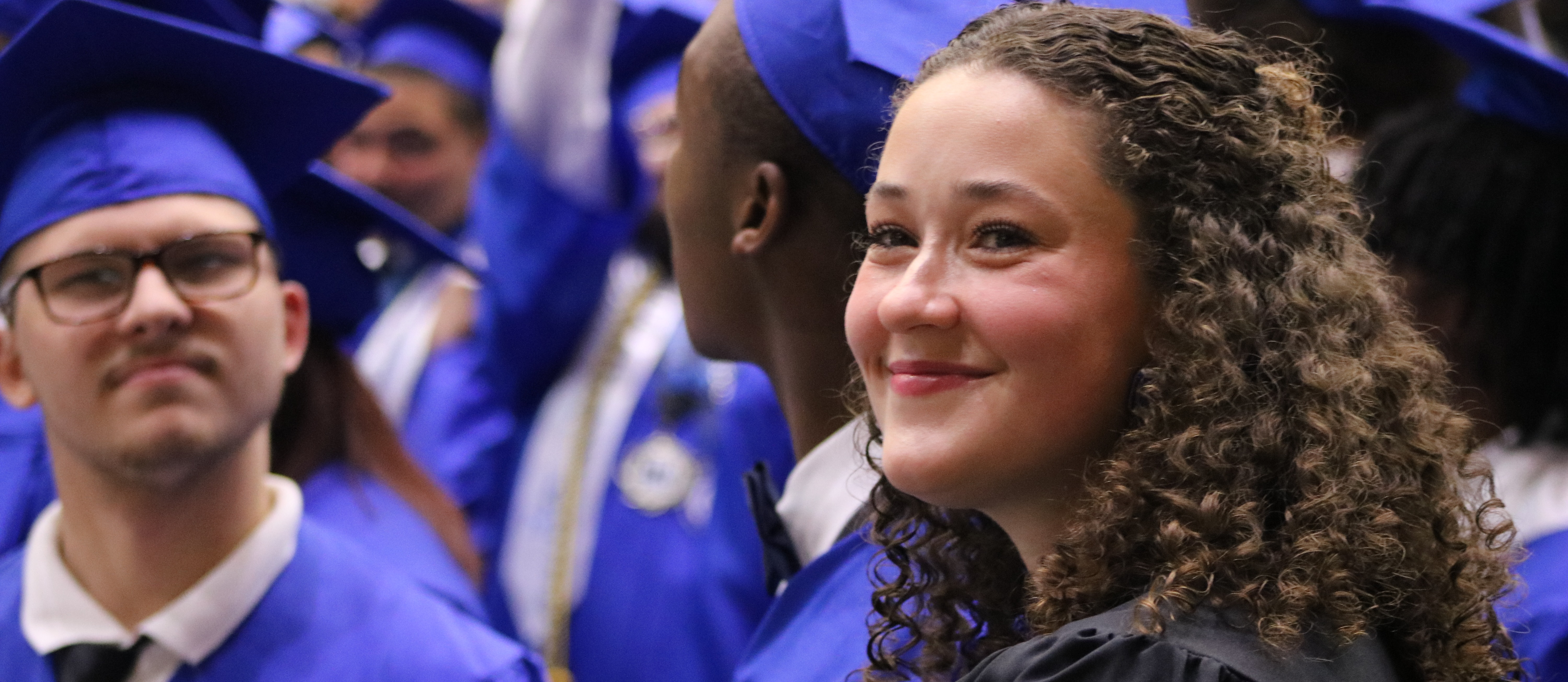 a woman looks over her shoulder as everyone waits to graduate in the background.