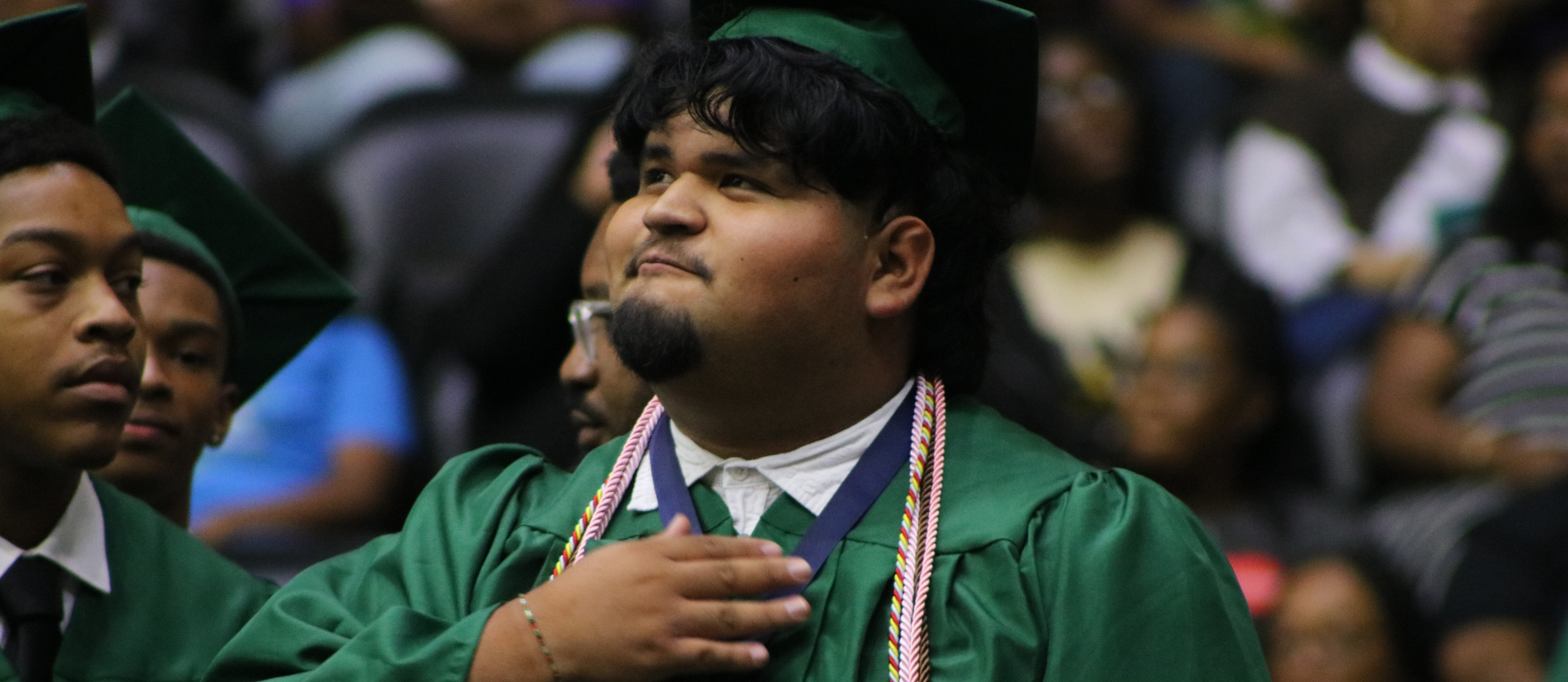 a person with his hand on chest in graduation regalia.