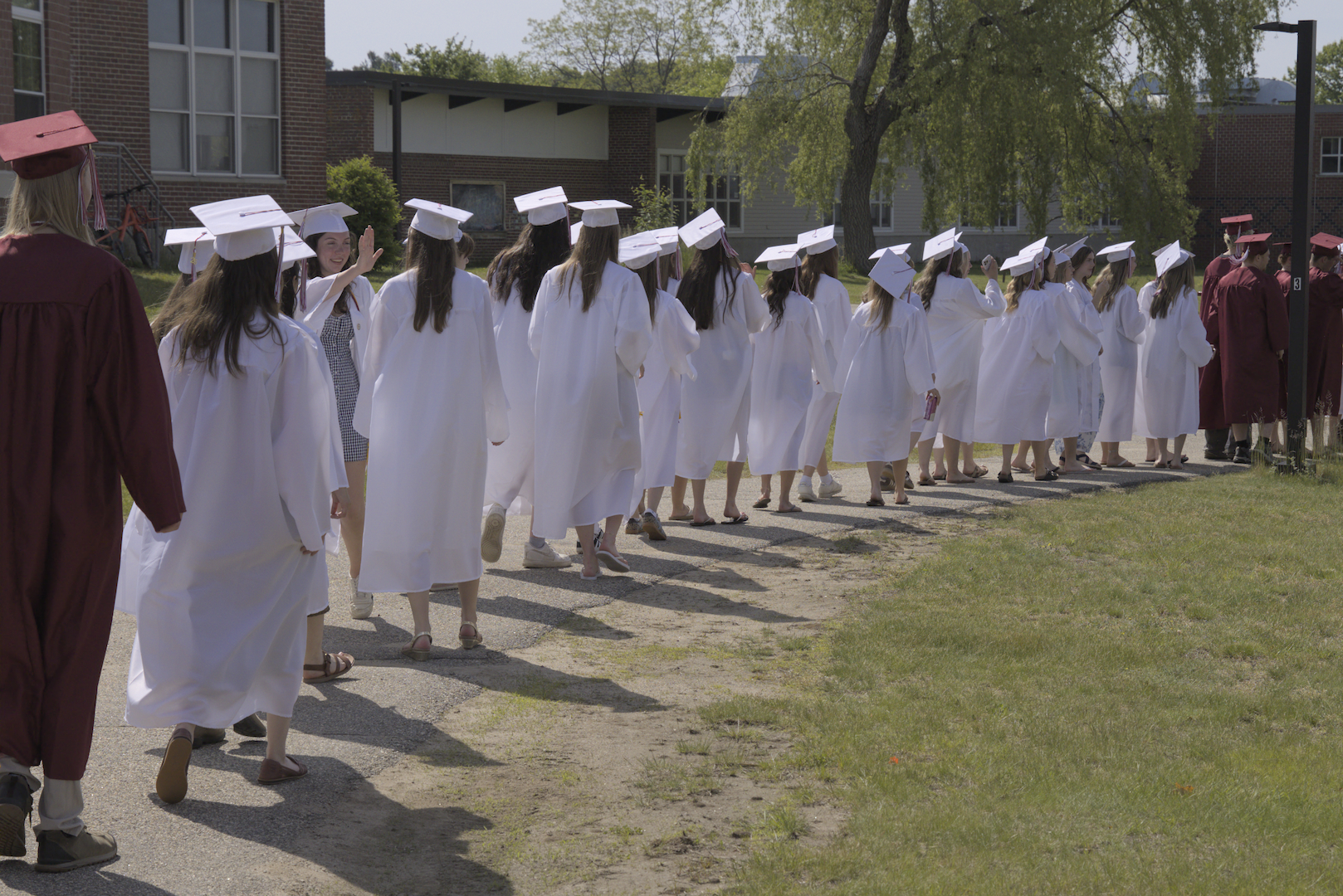 Seniors in Cap &amp; Gowns walk along a path. 