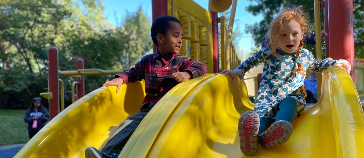Two children sliding down a playground slide