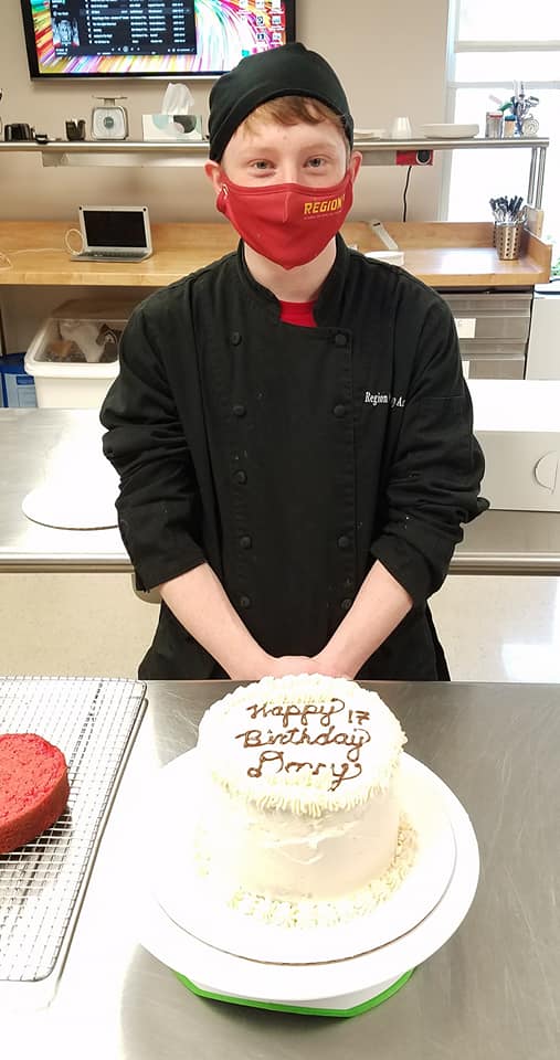 Young man poses behind a decorated birthday cake