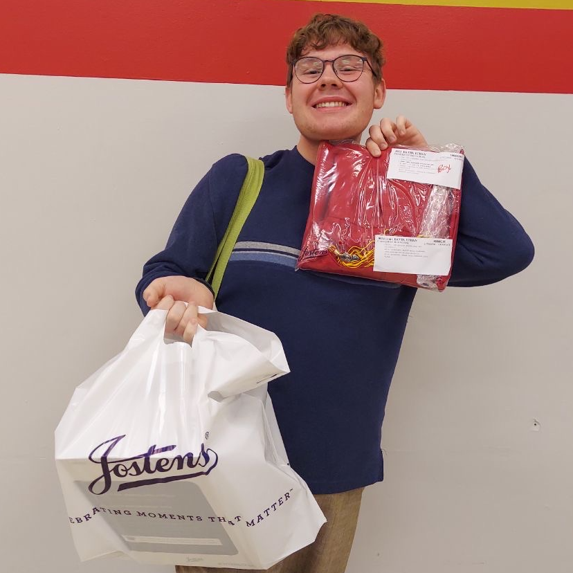 Senior Ethan holding cap and gown and bag while smiling
