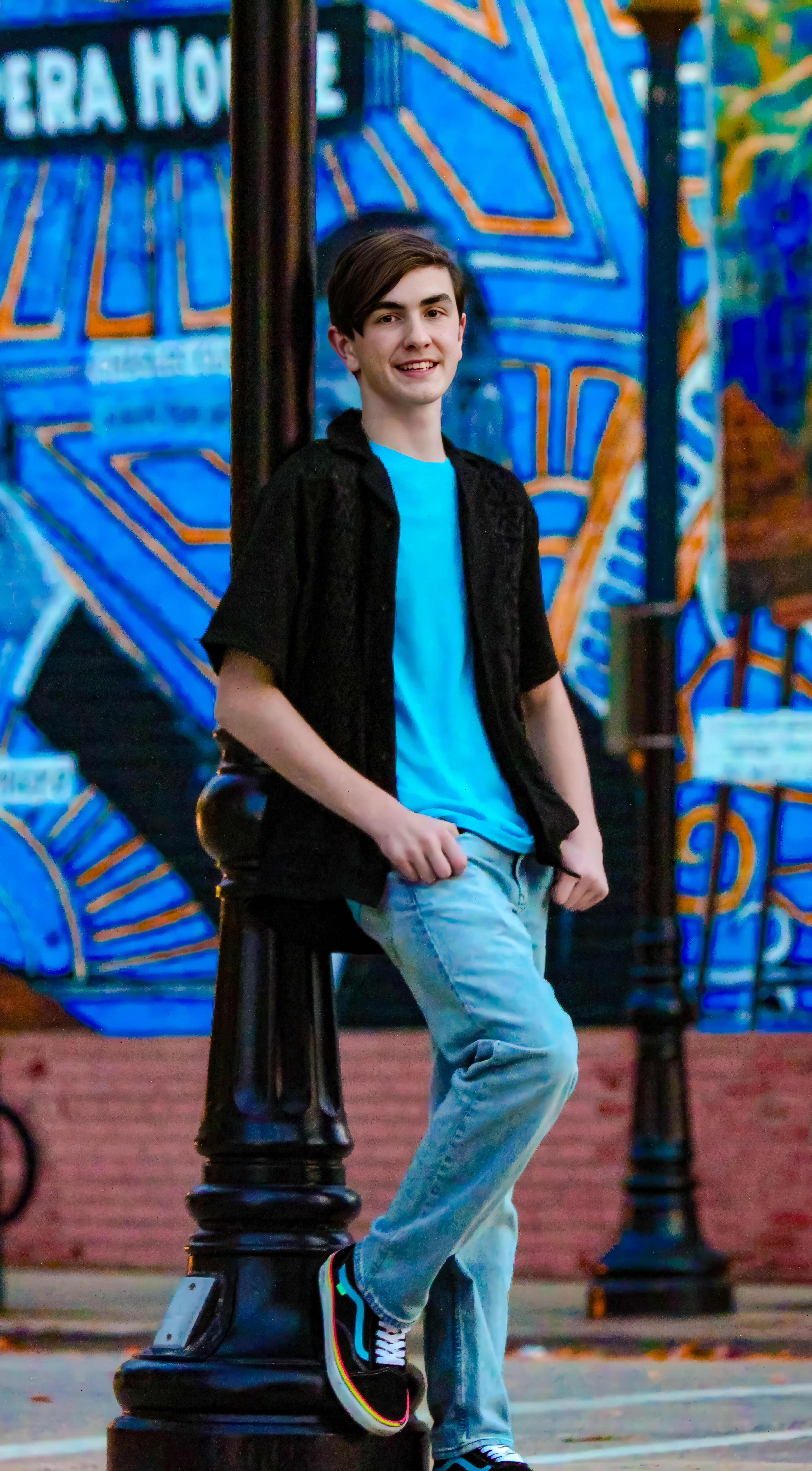 Black haired boy in blue top, black over shirt, and jeans leaning against pole. Henry Watson, Freshman, Bass