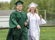 This is an image of two students walking in graduation cap and gown attire. One gown is white the other is green