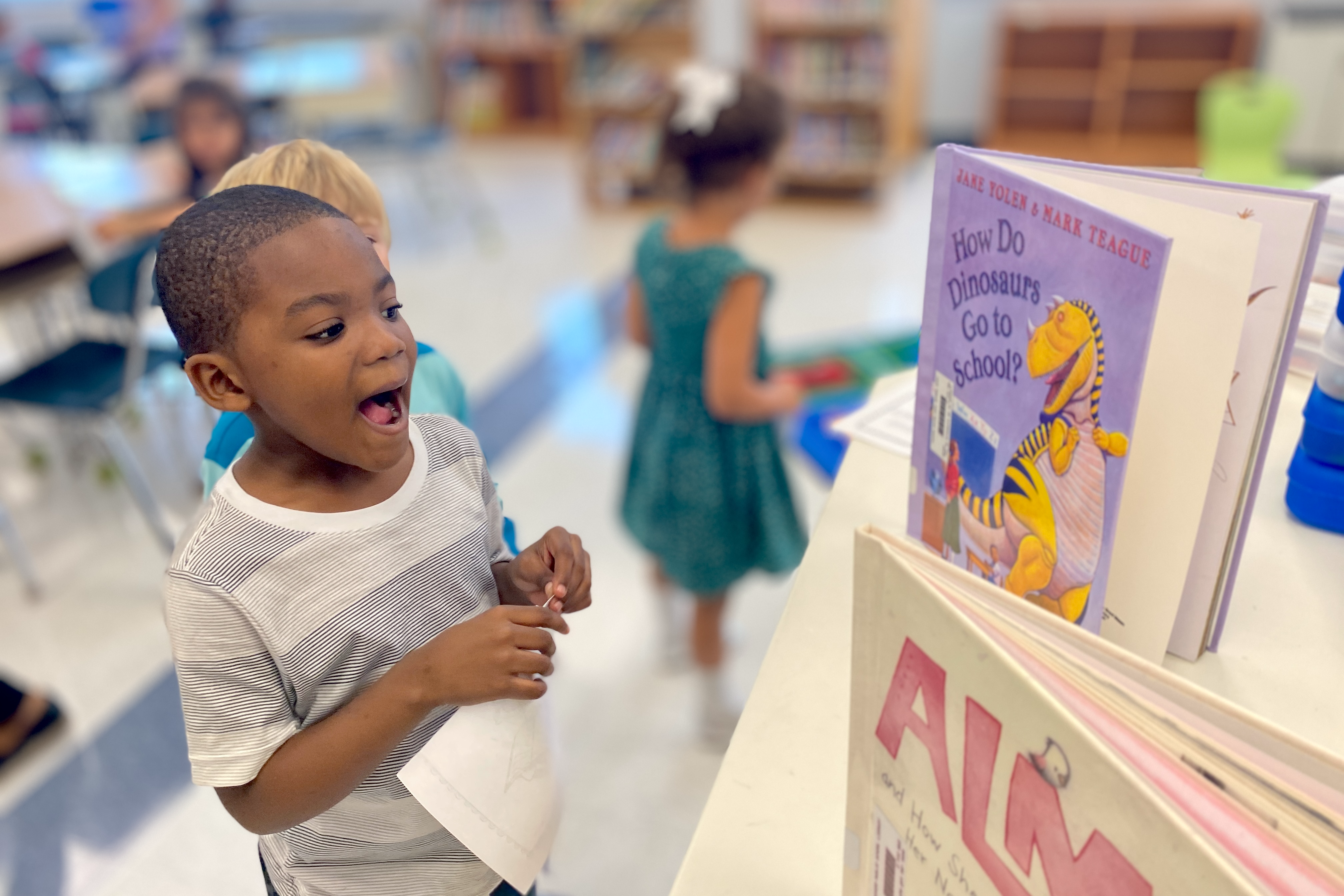 kindergarten student looking at book, "How do Dinosaurs Go to School"