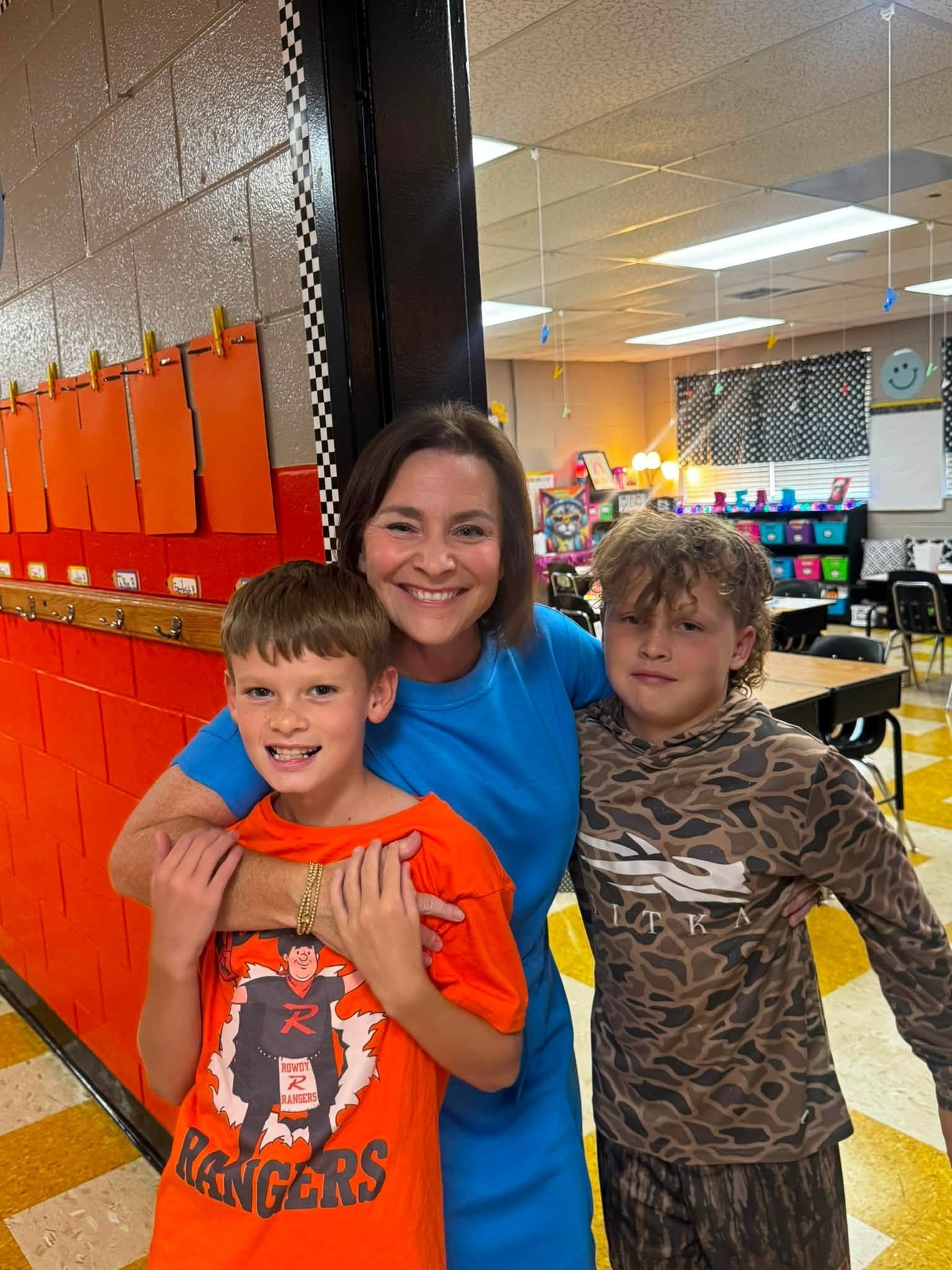 2 students posing for a photo in front of a classroom with a teacher