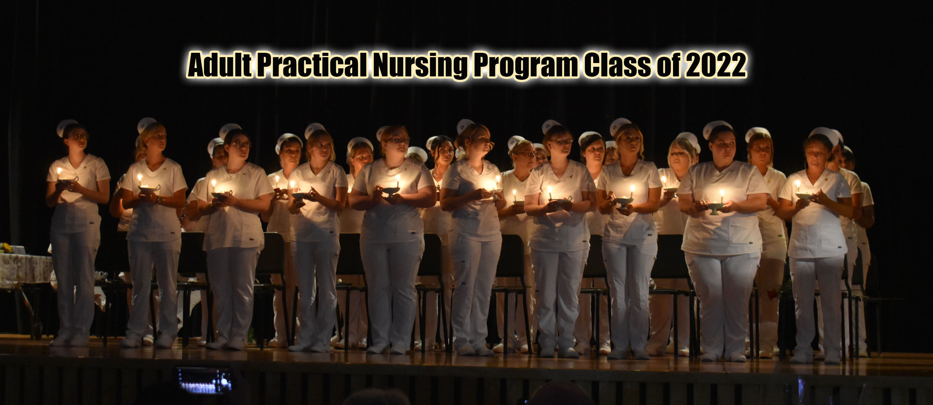 Adult LPN program graduates on stage for candle lighting ceremony