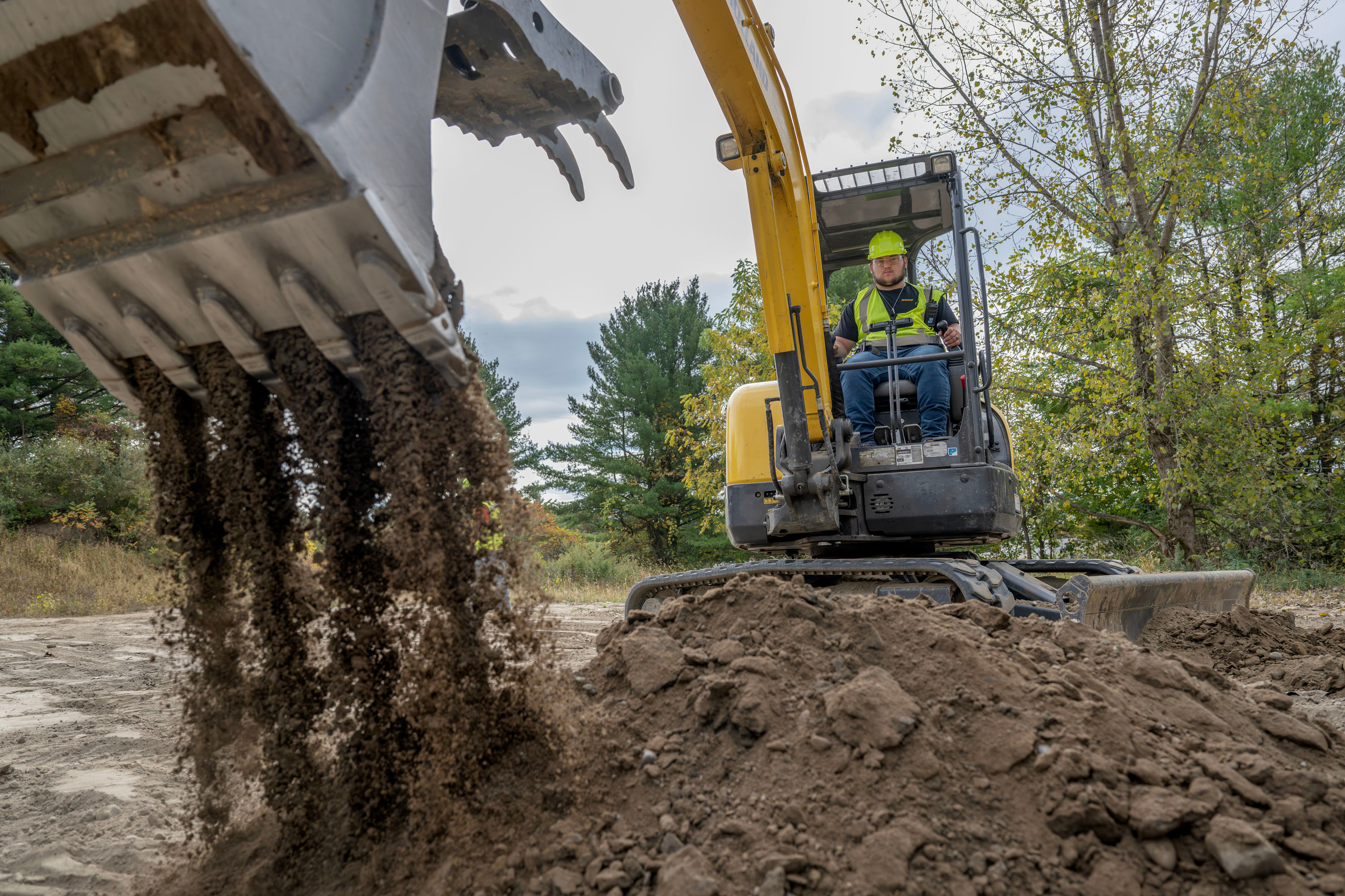 Heavy Equipment student operating machinery outside and scooping and dropping dirt