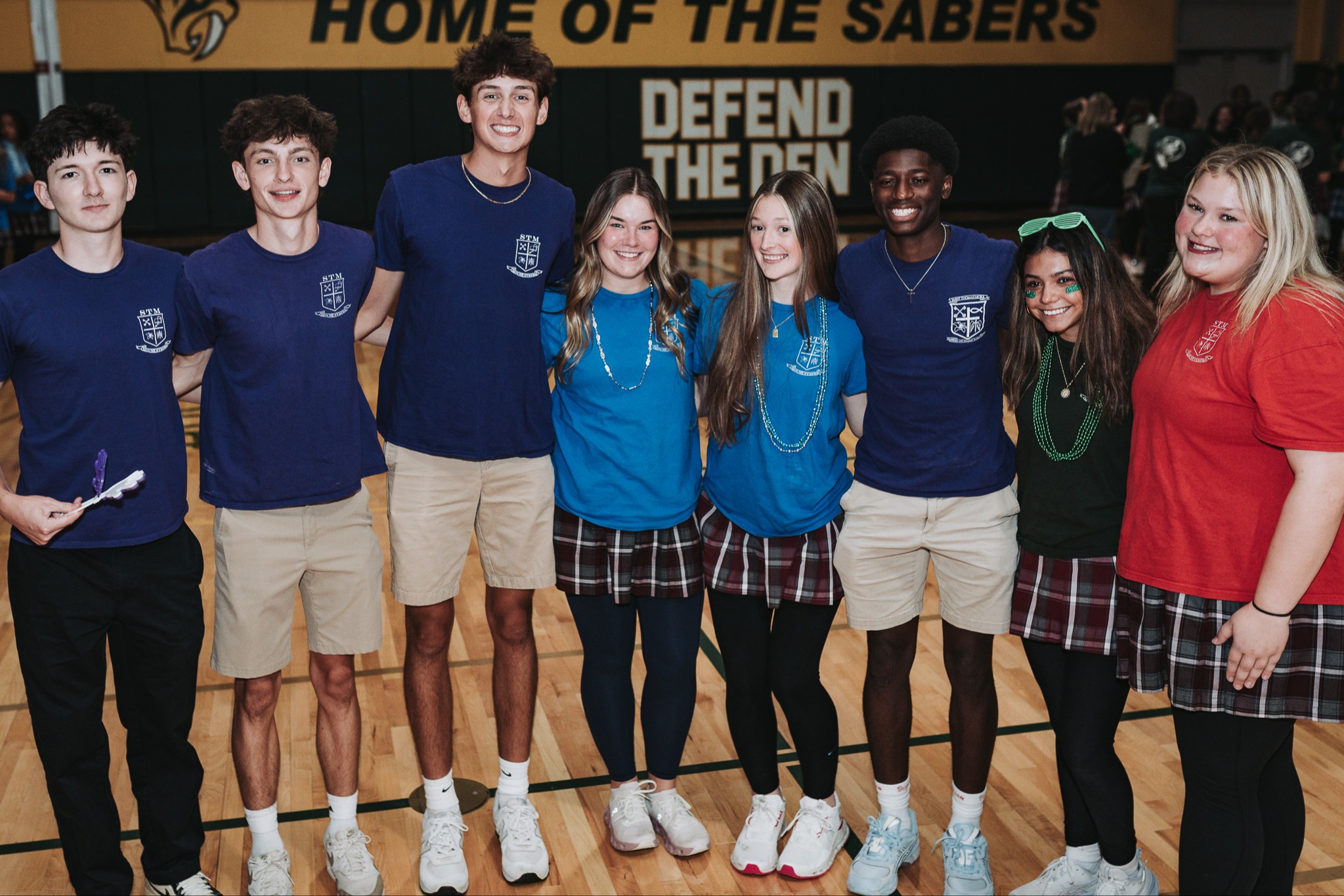 Group of people in blue shirts and shorts, posing for a photo on a basketball court.
