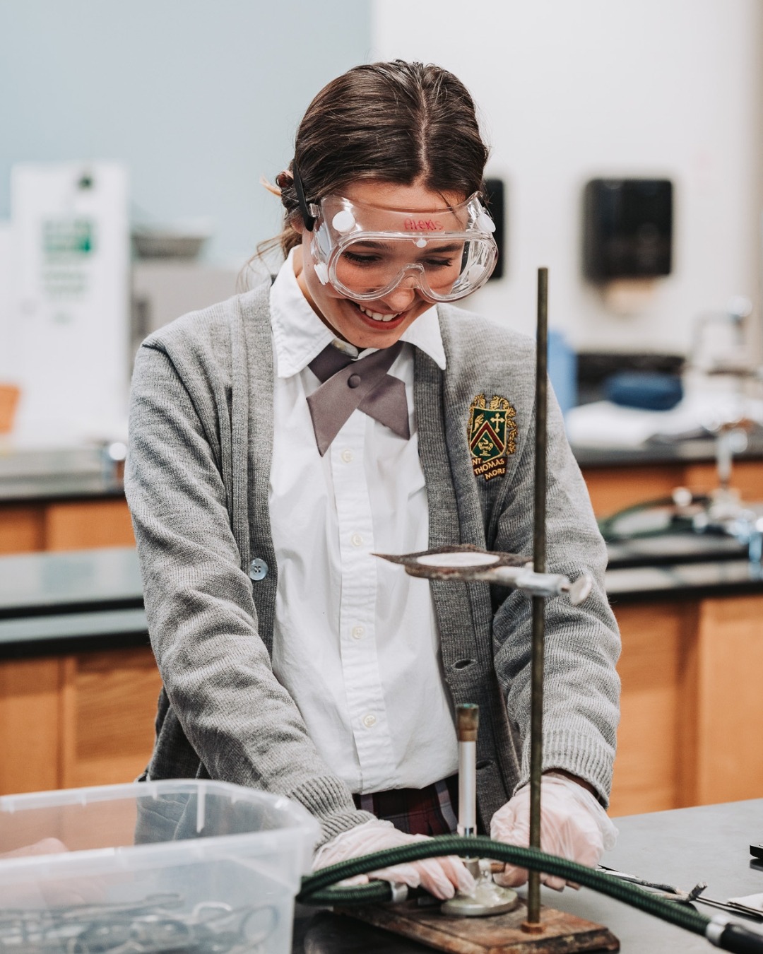 A student wearing a sweater and goggles in a science lab, working on a lab equipment.