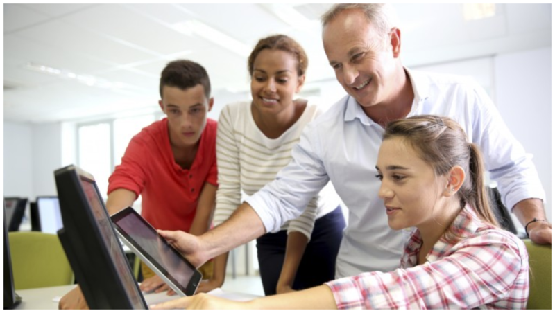 Photo of a teacher with 3 students teaching in his tablet.