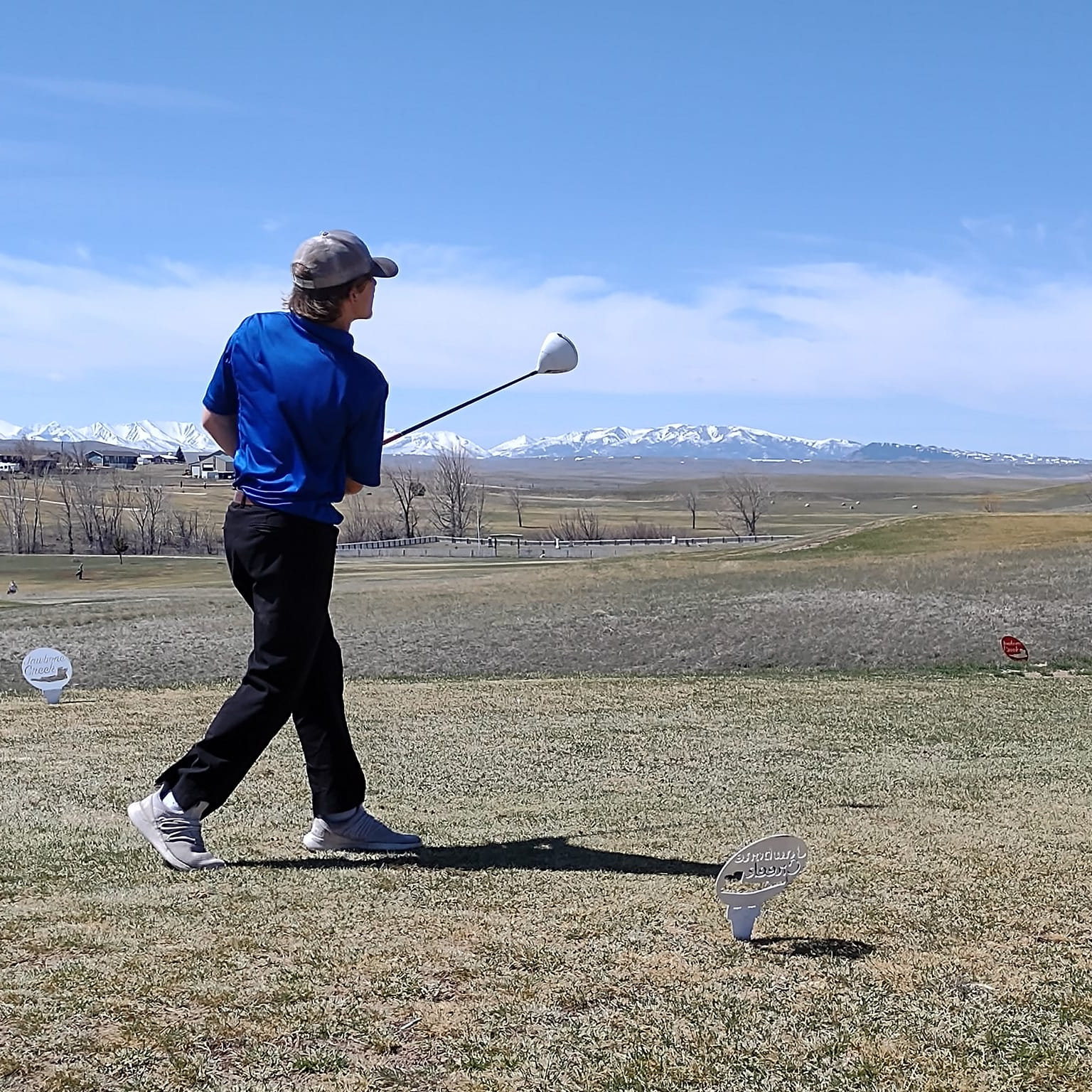 Male golfer in a blue collared shirt teeing off at a golf meet