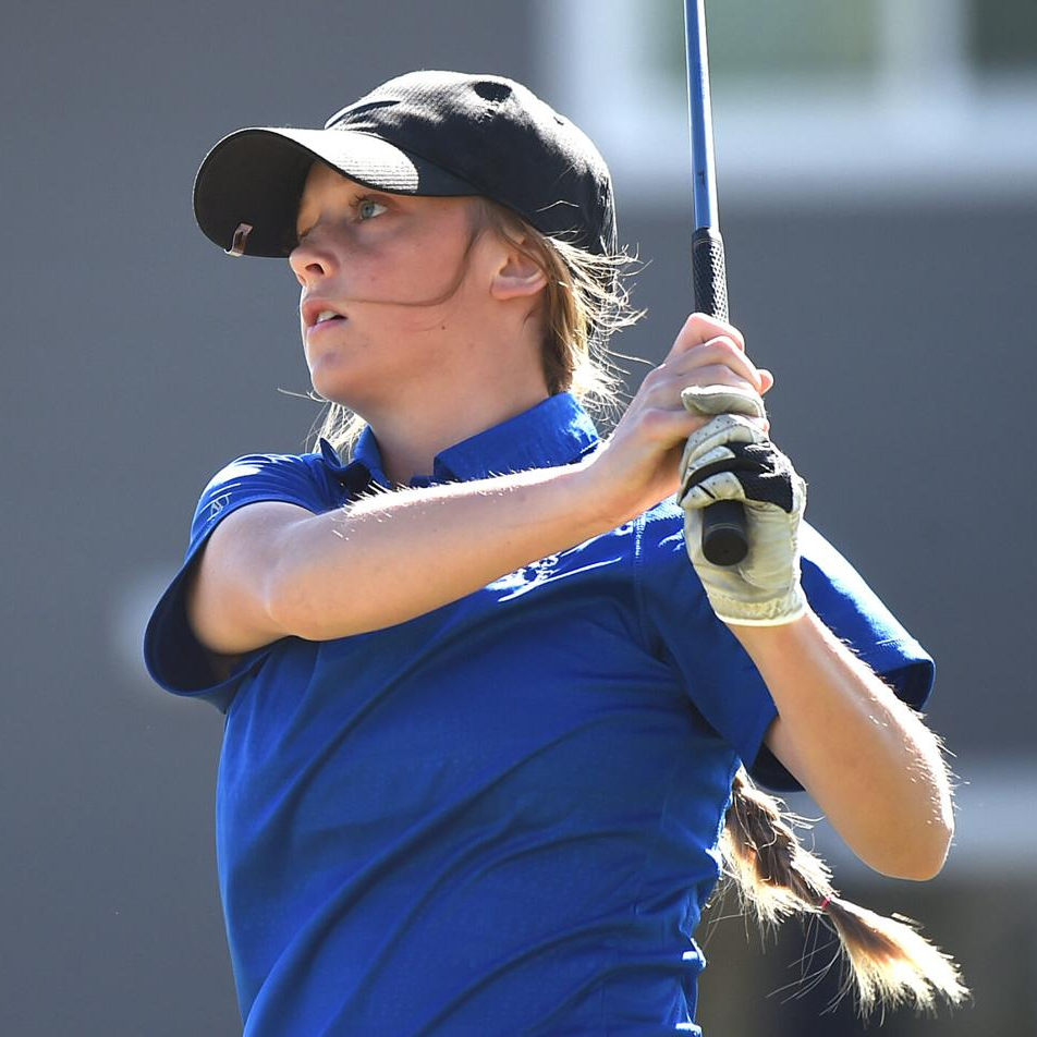 female golfer in a blue collared short and black hat follows through on a swing during a golf meet